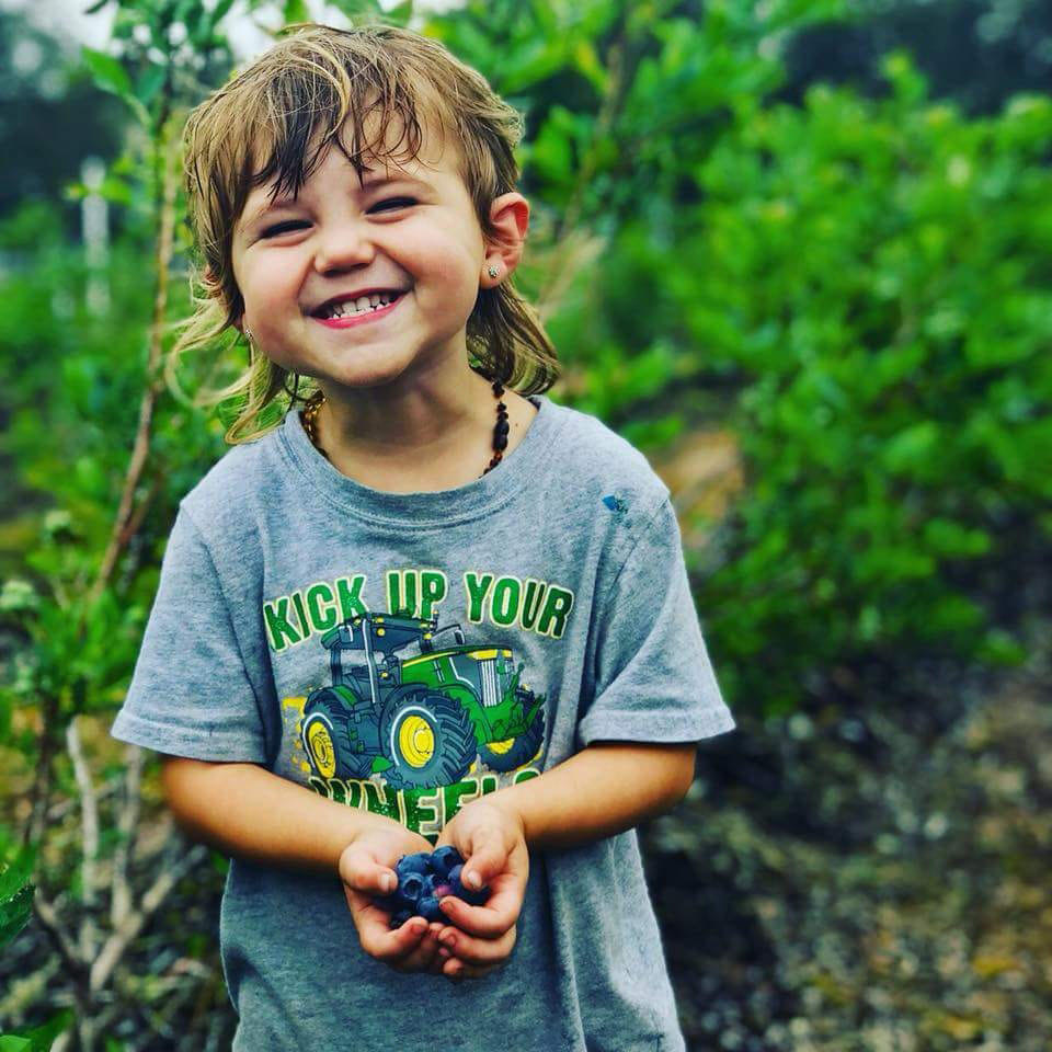 kid picking blueberries with a big smile